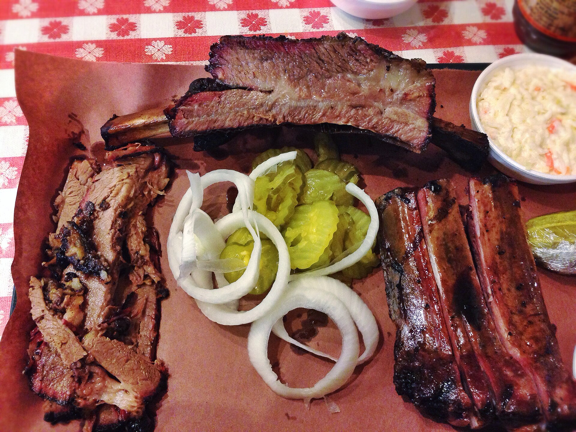 A Central Texas barbecue plate of sliced brisket, ribs, pickles and onion on butcher paper