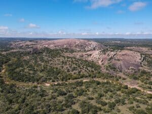 Aerial view of the pink granite dome of Enchanted Rock rising above oak and juniper scrub in the Texas Hill Country