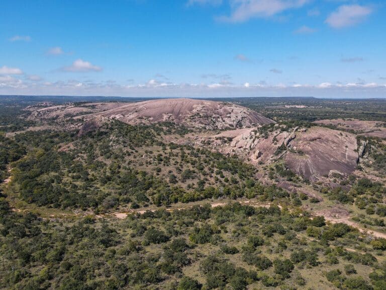 Aerial view of the pink granite dome of Enchanted Rock rising above oak and juniper scrub in the Texas Hill Country