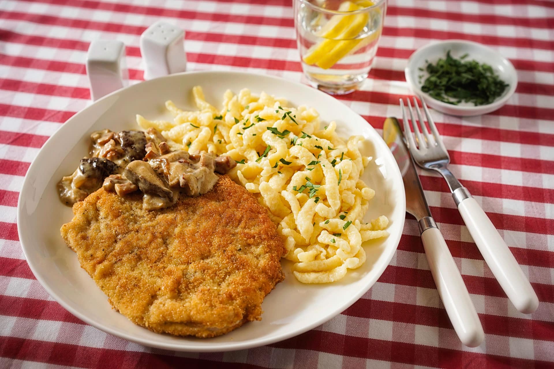 A plate of breaded schnitzel with spaetzle and mushroom sauce on a checked tablecloth