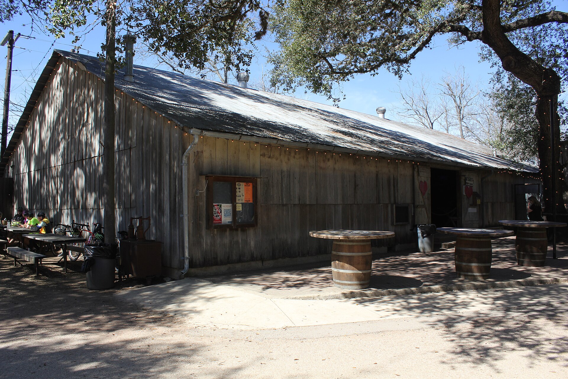 The weathered timber Luckenbach dance hall with wine-barrel tables and string lights under live oak trees